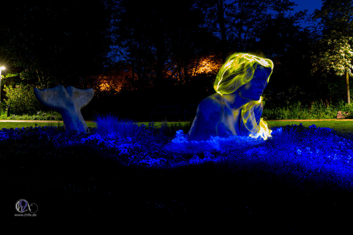 Frau mit Schleier und Lichtkranz in mystischer Pose vor Wasser